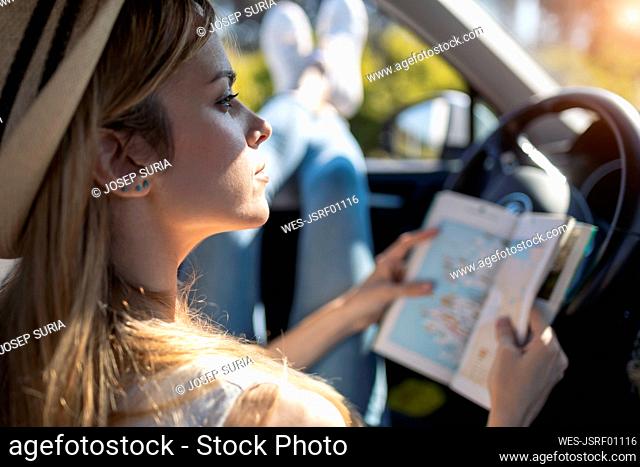 Young woman holding travel guide while sitting in car