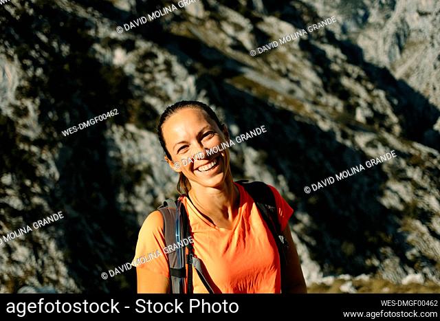 Happy woman with backpack standing against mountain at Cares Trail in Picos De Europe National Park, Asturias, Spain