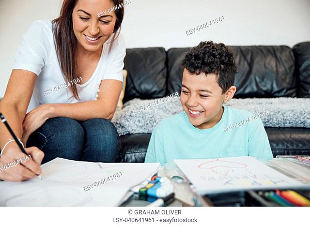 Little boy and his mother are making a Father's Day card at home using crayons and paints
