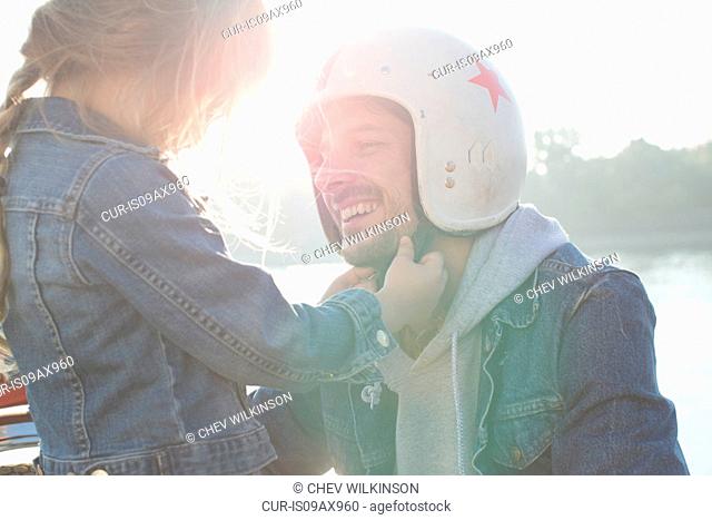 Young girl helping her father put on crash helmet
