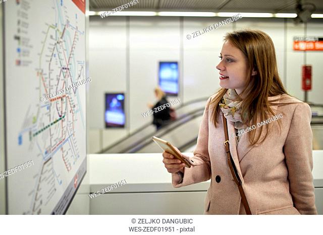 Austria, Vienna, smiling young woman looking at map at underground station