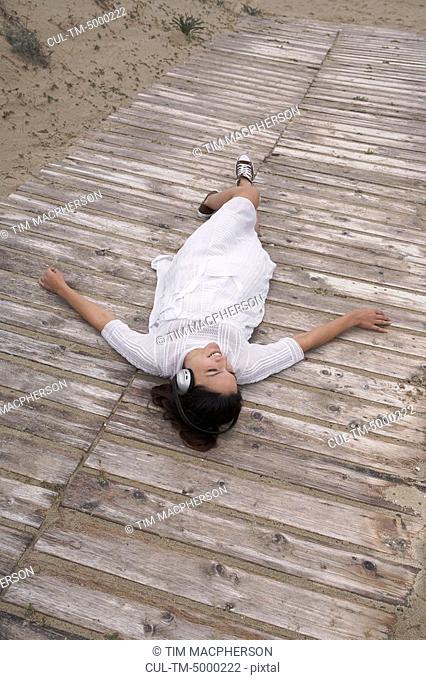 Woman wearing headphones lying on boardwalk