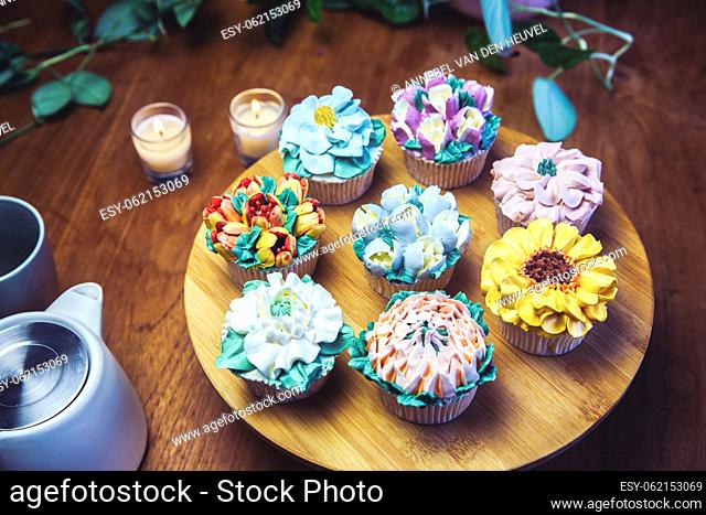 Various cupcakes decorated with colorful flower icing on wooden table, floral bouquet, wedding cake, High tea, Holiday concept Mothers day