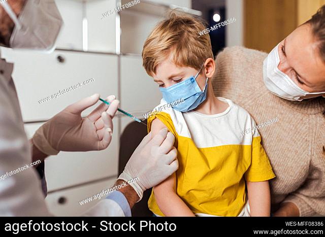 Mother looking at son getting vaccinated by doctor in center