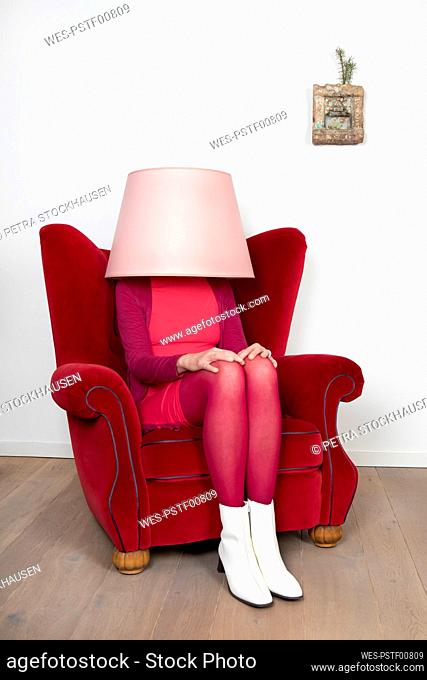 Woman sitting on armchair while face covered with lamp shade