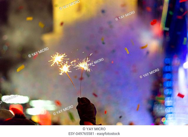 New Year celebration on main square. A lot of smoke or fog, lights, salute and confetti. Blurred colorful background. Bengali fire in hand with glove on...