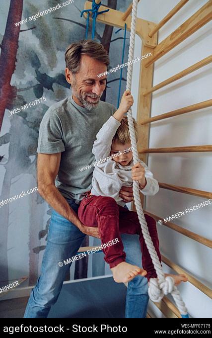 Father assisting son climbing rope at home