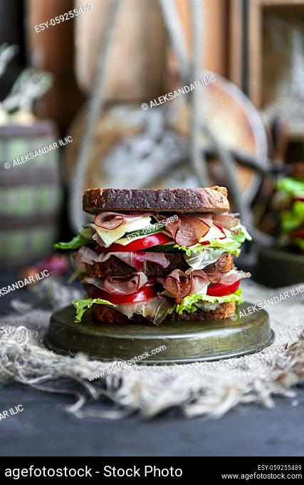 Big sandwich with bread, prosciutto, lettuce, tomtatoes, cucumber and cheese in the kitchen