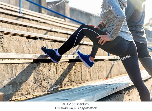 fitness, sport, exercising and lifestyle concept - close up of couple stretching leg on stands of stadium