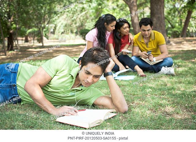 Friends listening to mp3 player and studying in a park, Lodi Gardens, New Delhi, Delhi, India