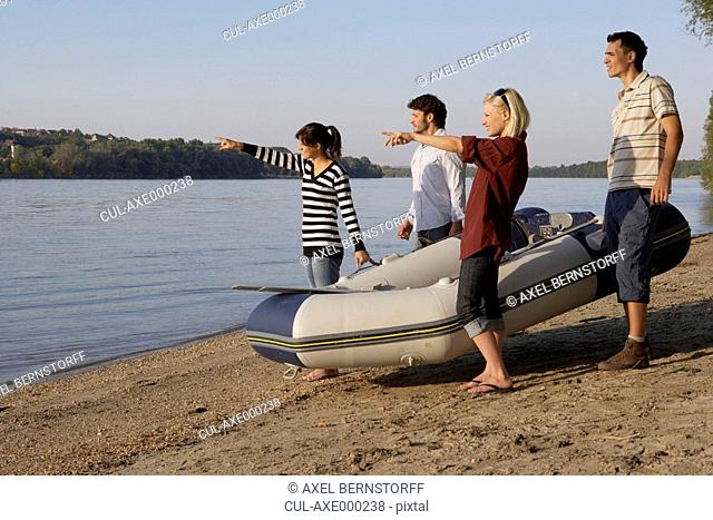 Four friends with a raft on a beach smiling and pointing