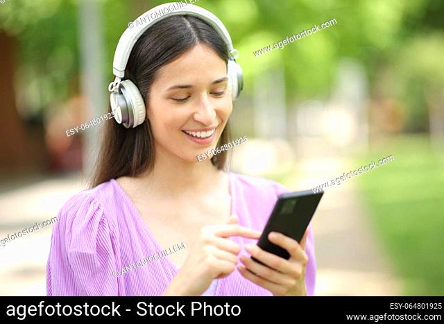 Happy woman listening to music on cell phone walking in a park