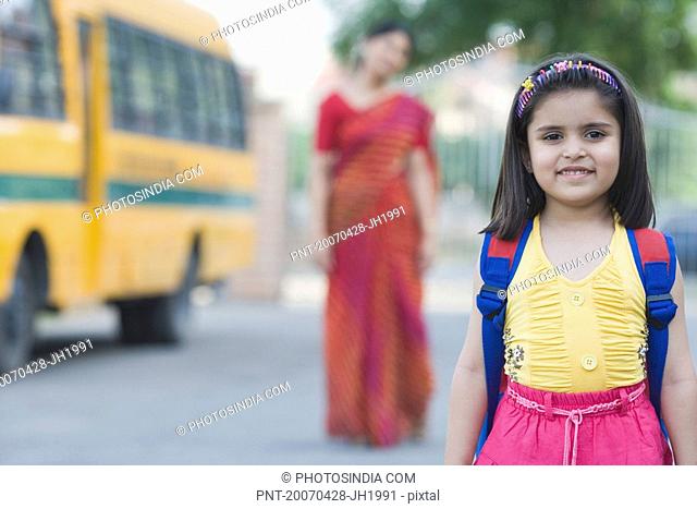 Portrait of a schoolgirl smiling with her teacher standing in the background