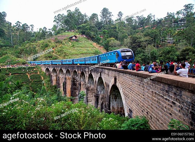 Demodara, Sri Lanka - August 5, 2018: People next to a blue train crossing the famous Nine Arch Bridge