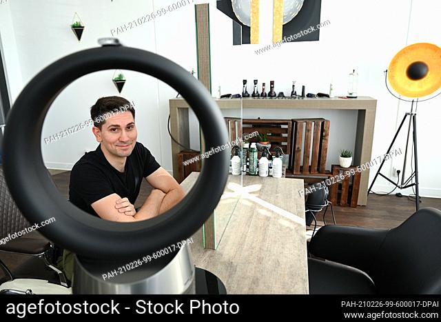 23 February 2021, Hessen, Seeheim-Jugenheim: Konstantin Schick, owner of the salon ""Schick Friseure"", sits behind a fan in his shop