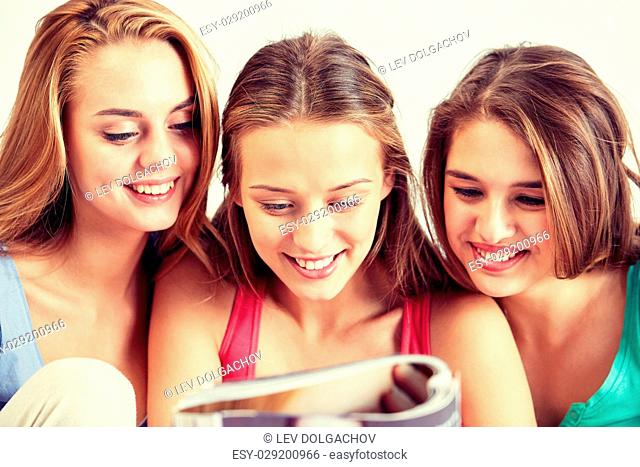 friendship, people and pajama party concept - happy friends or teenage girls reading magazine at home