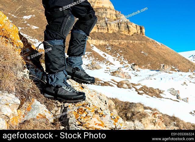 Close-up of a tourist's foot in trekking boots with sticks for Nordic walking standing on a rock stone in the caucasian mountains