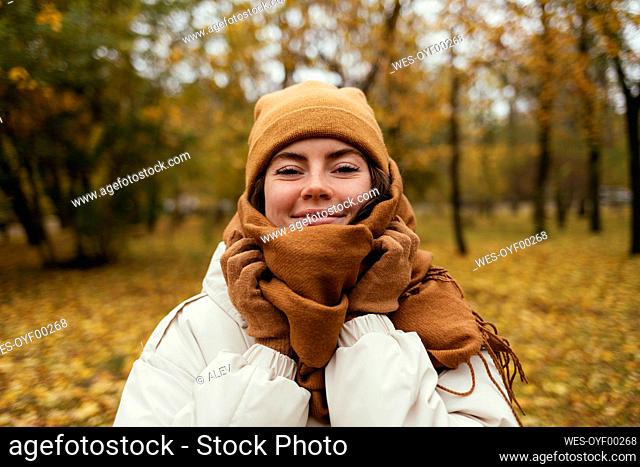 Smiling young woman wrapped up in scarf in autumn park