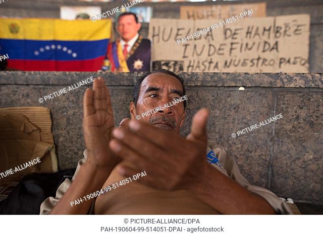 04 June 2019, Venezuela, Caracas: A man claps his hands against the background of a Venezuelan flag and a portrait of the late head of state Hugo Chavez in a...