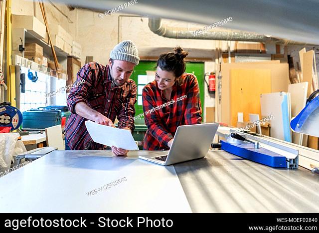 Craftswoman and craftsman with plan and laptop discussing in their workshop