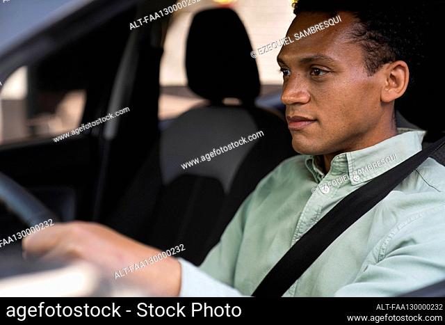 Mid-shot portrait taken from outside the vehicle of African-American businessman driving his car to work
