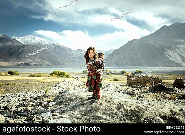 Girl carrying her little brother on her back, members of the ethnic group of sedentary Wakhi, Saradh-e-Broghil, Wakhan Corridor, Afghanistan, Asia