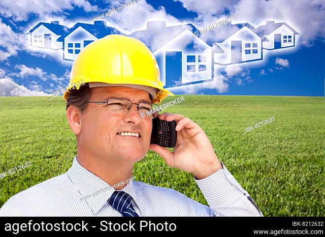 Contractor in hardhat on his cell phone over house icon, empty grass field and deep blue sky with clouds