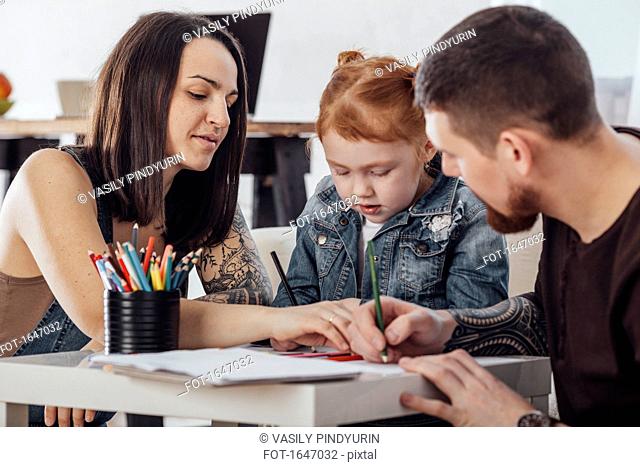 Parents drawing with daughter while sitting in living room at home