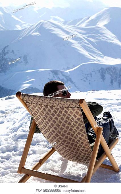 Skier at winter mountains resting on sun-lounger at nice sun day. Caucasus Mountains, Georgia, region Gudauri