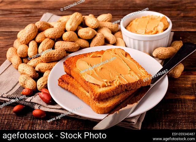 Peanut butter sandwich on plate with inshell peanuts, breakfast on the wooden background