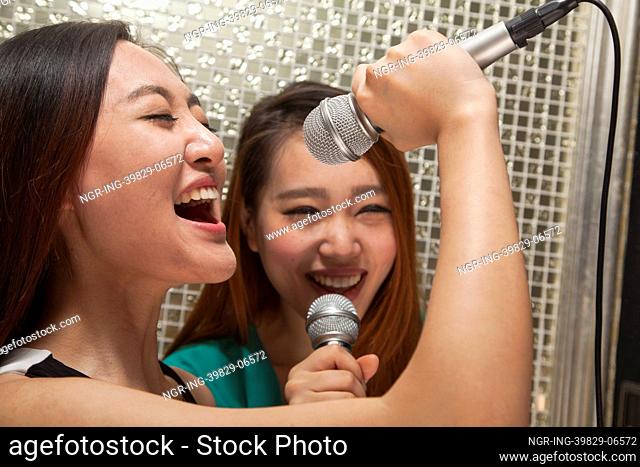 Two young female friends singing into a microphone at karaoke