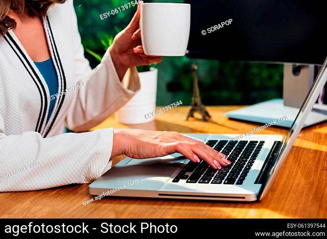 Beautiful business woman lifestyle working using laptop computer and holding coffee cup on hand while enjoying in modern desk office near window