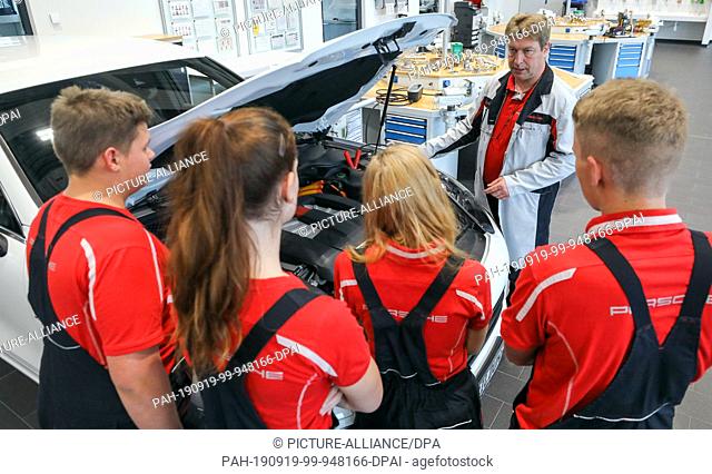 09 September 2019, Saxony, Leipzig: Instructor Carsten Pohle (in a smock) explains the functionality of a hybrid drive on a Cayenne Hybrid at the Porsche...