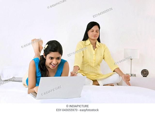 Girl with laptop while mother meditates