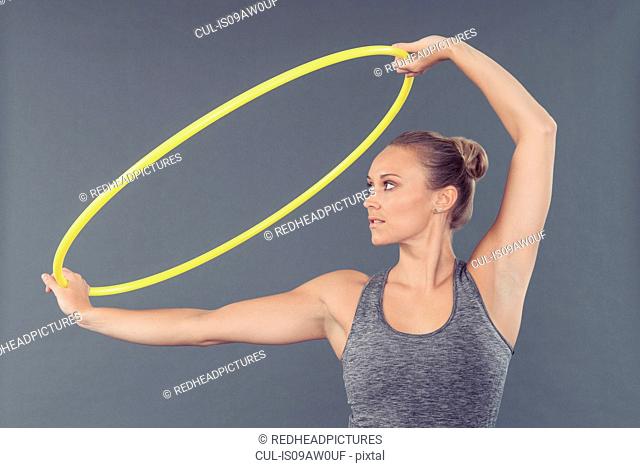 Young woman practising with hula hoop, grey background