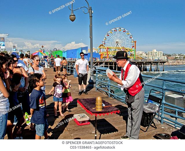 An elderly magician shuffles cards for his audience in the amusement park on Santa Monica Pier