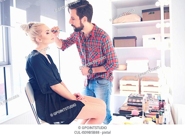 Male make up artist applying eyeliner to model for photo shoot
