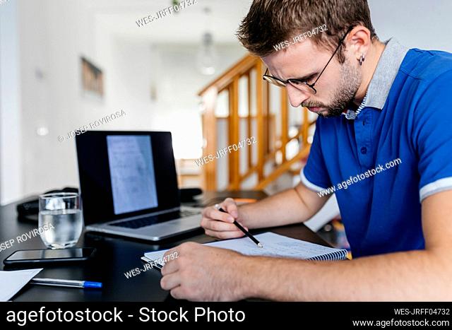 Dedicated young male university student doing math at home