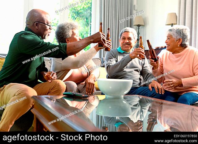 Two diverse senior couples sitting on sofa with beer and having fun