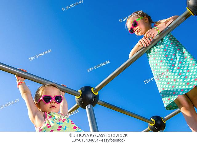 Two young girls on the jungle gym, sunny day