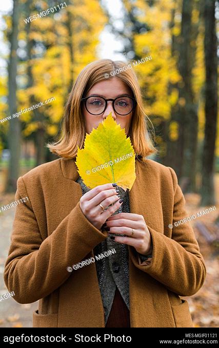 Woman holding autumn leaf in front of mouth at park