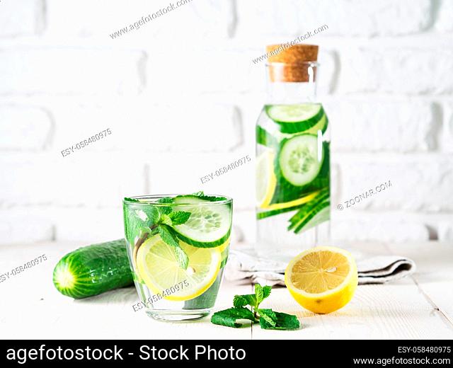 Infused detox water with cucumber, lemon and mint in glass and bottle on white table. Diet, healthy eating, weight loss concept. Copy space