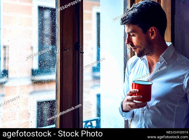 Young man holding cup looking out of window