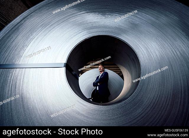 Thoughtful businessman with arms crossed standing at rolled up metal sheet