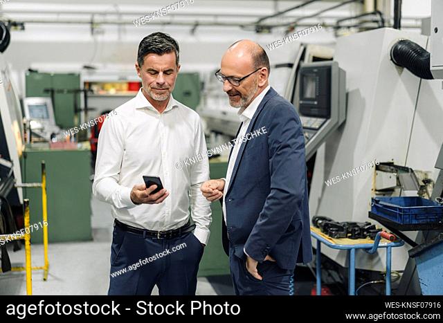 Two businessmen using smartphone in a factory