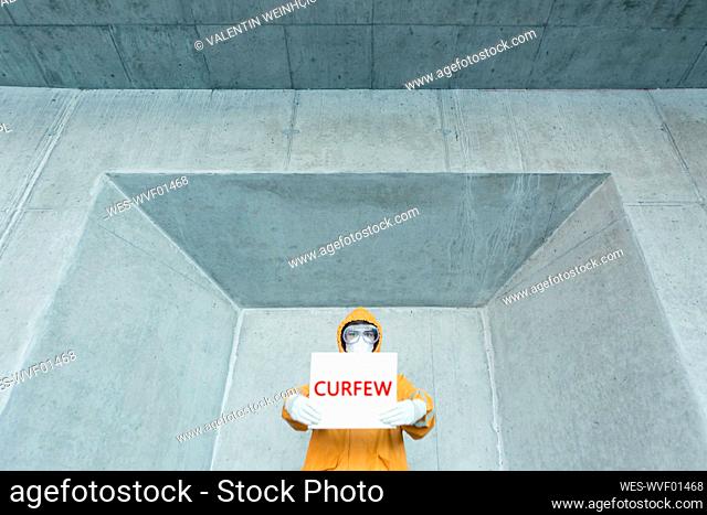 Portrait of man wearing protective clothing holding a 'curfew' sign