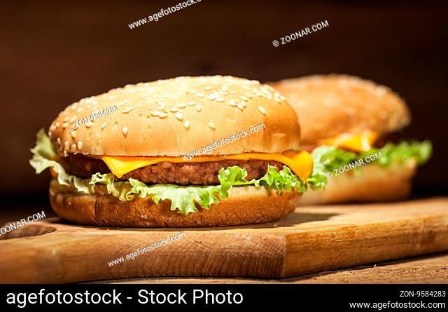 Fresh delicious burgers with cheese, onion and lettuce wooden background