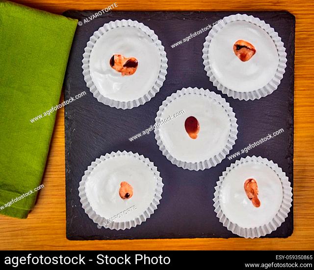 Several Raw French dessert Meringues with Strawberry sauce decorated with a napkin on a wooden table and a black slate board. Top View