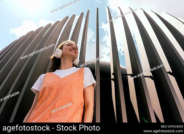 Smiling woman listening music through headphones in front of wooden wall