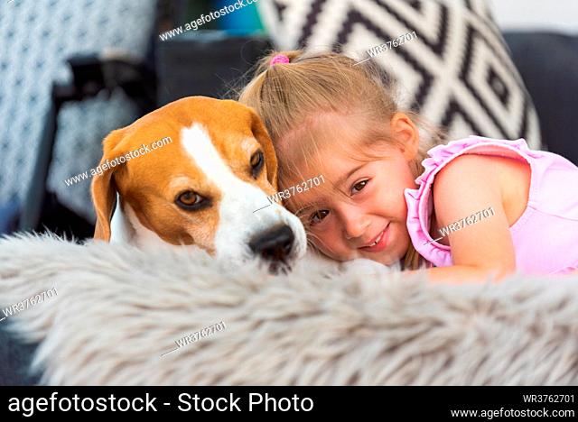 Child cuddle a dog on backyard sofa. Happy childhood with beagle pet